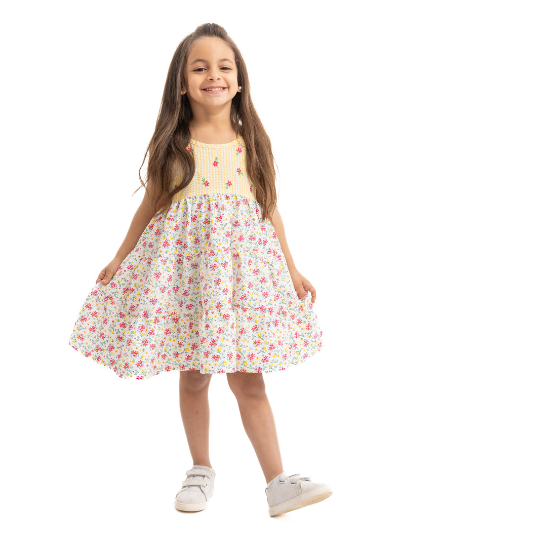 A young girl wearing a sleeveless floral printed dress in summer colors, standing against a white background.